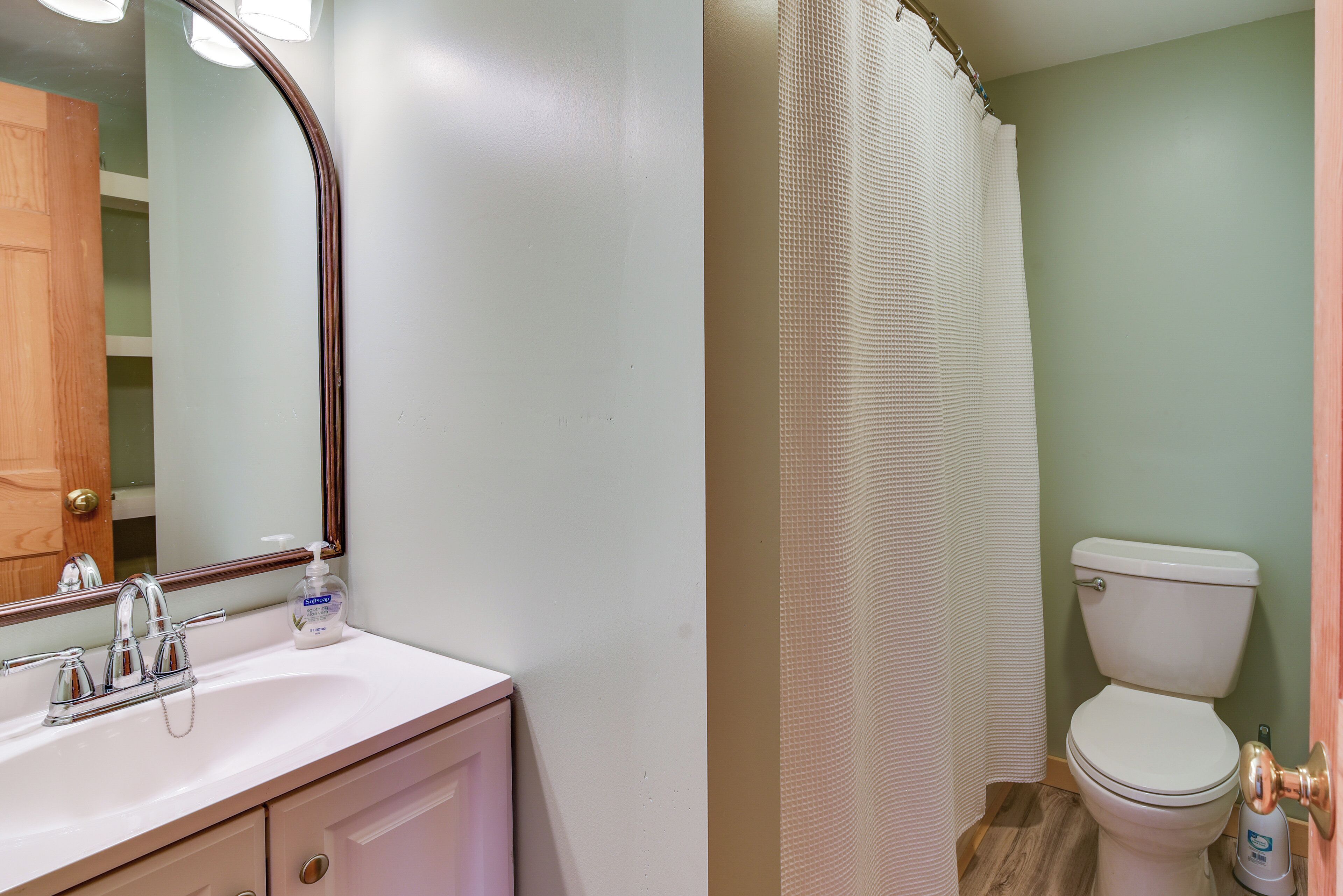 Un bagno con un lavandino bianco, uno specchio, un water e una tenda per la doccia.