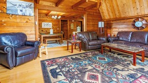 Ein Blockhaus-Interieur mit Ledersofas, einem Holztisch, einem gemusterten Teppich und einer Uhr an der Wand.