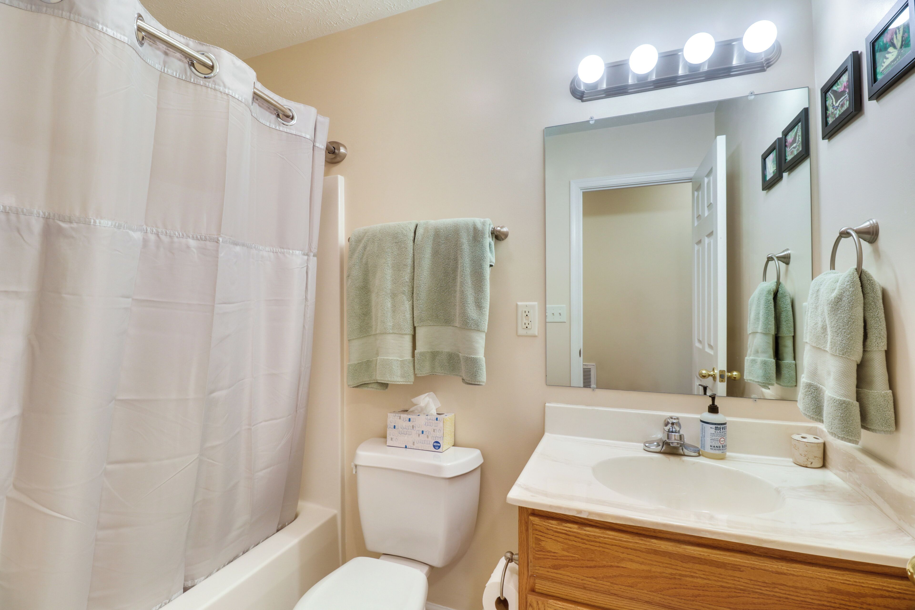 A bathroom with a white bathtub, a toilet, a sink, and a mirror with lights above.