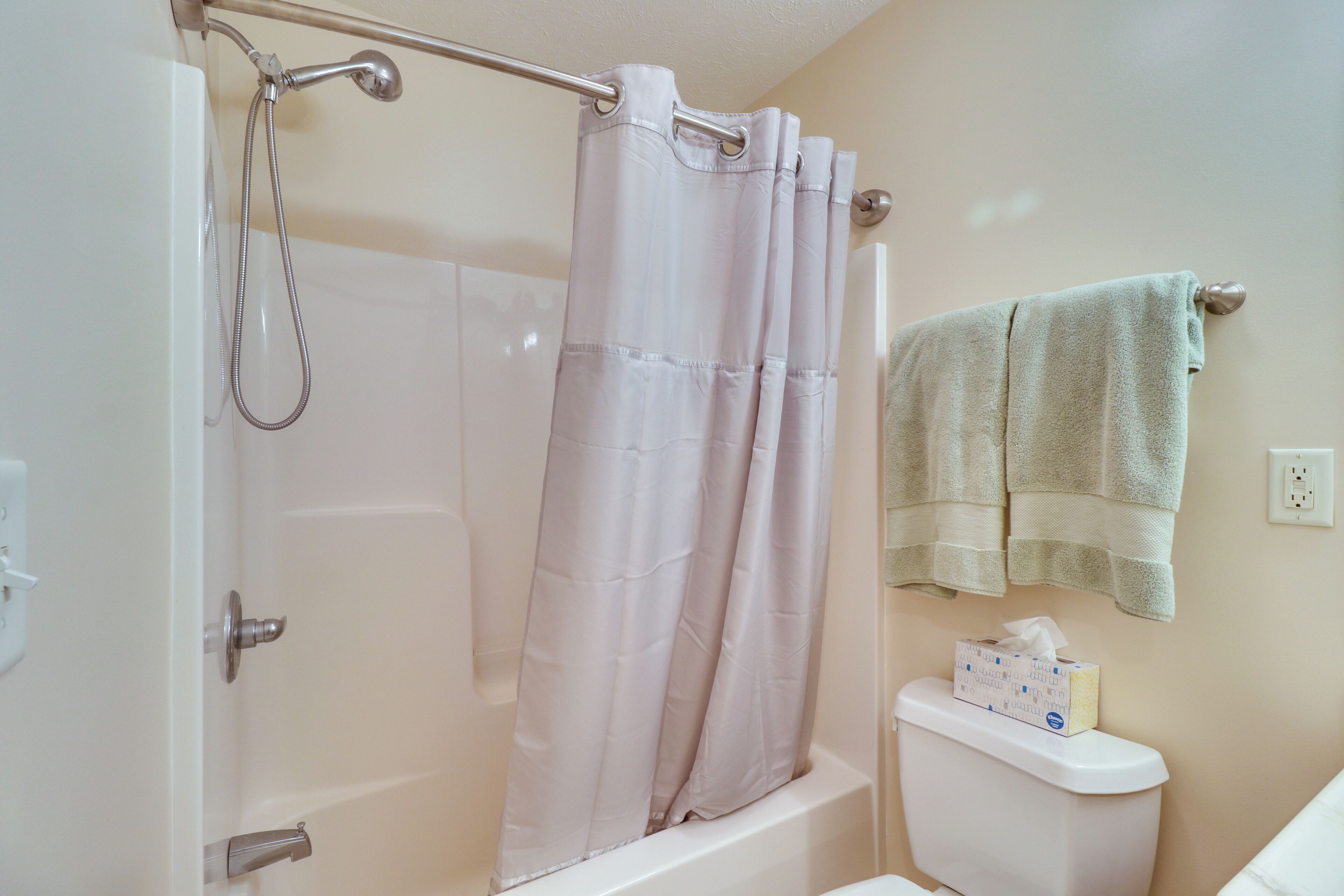 A bathroom with a shower curtain, a towel rack with a towel, and a toilet with a tissue box on it.