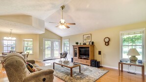 A spacious living room with a sofa, coffee table, and TV. There are multiple windows and a ceiling fan.