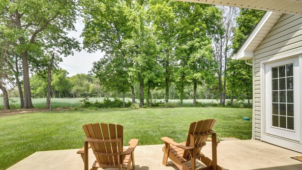 Two Adirondack chairs on a concrete patio with a view of a grassy yard and trees.