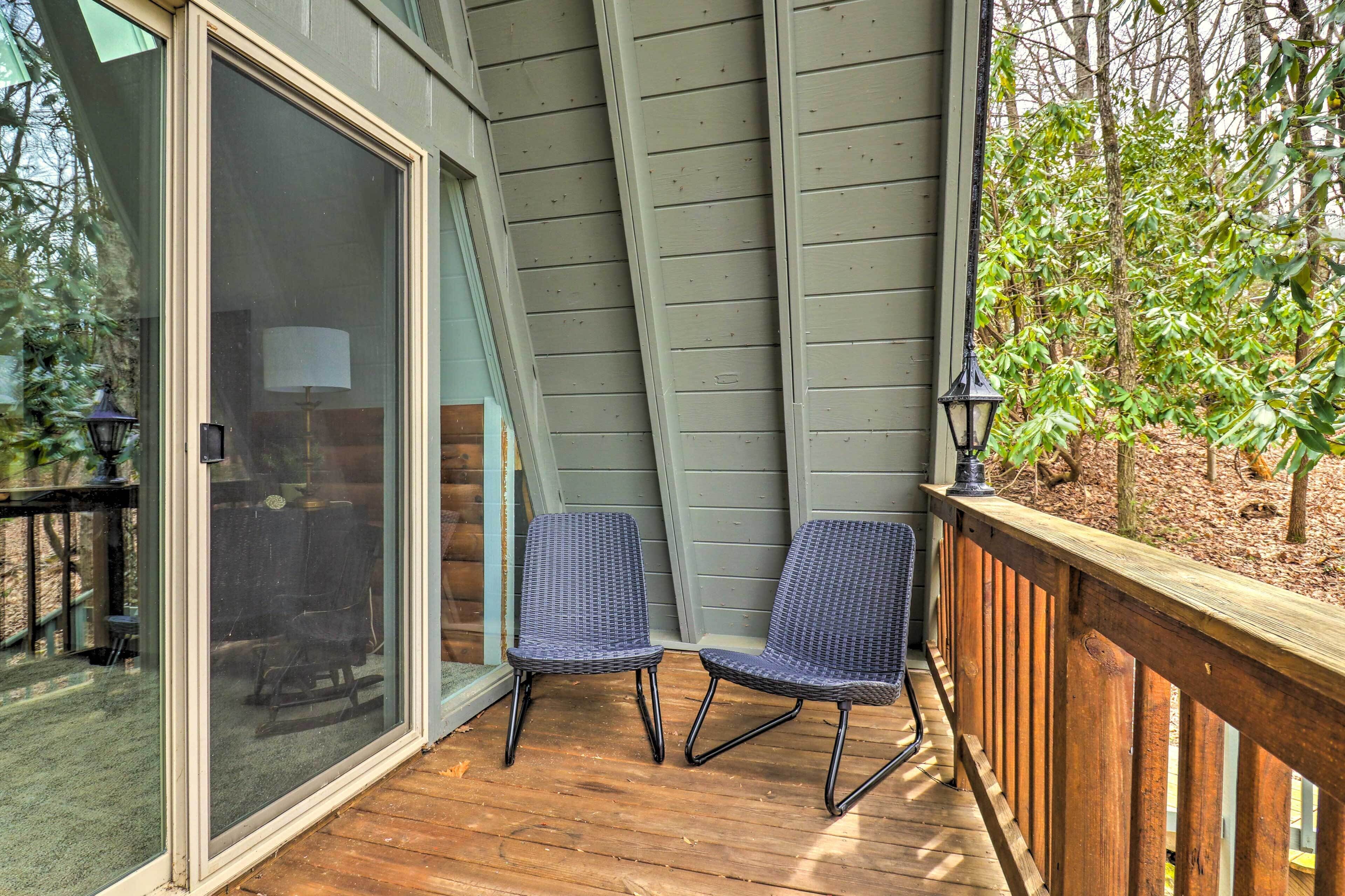 A wooden deck with two wicker chairs and a glass door leading to a patio area.