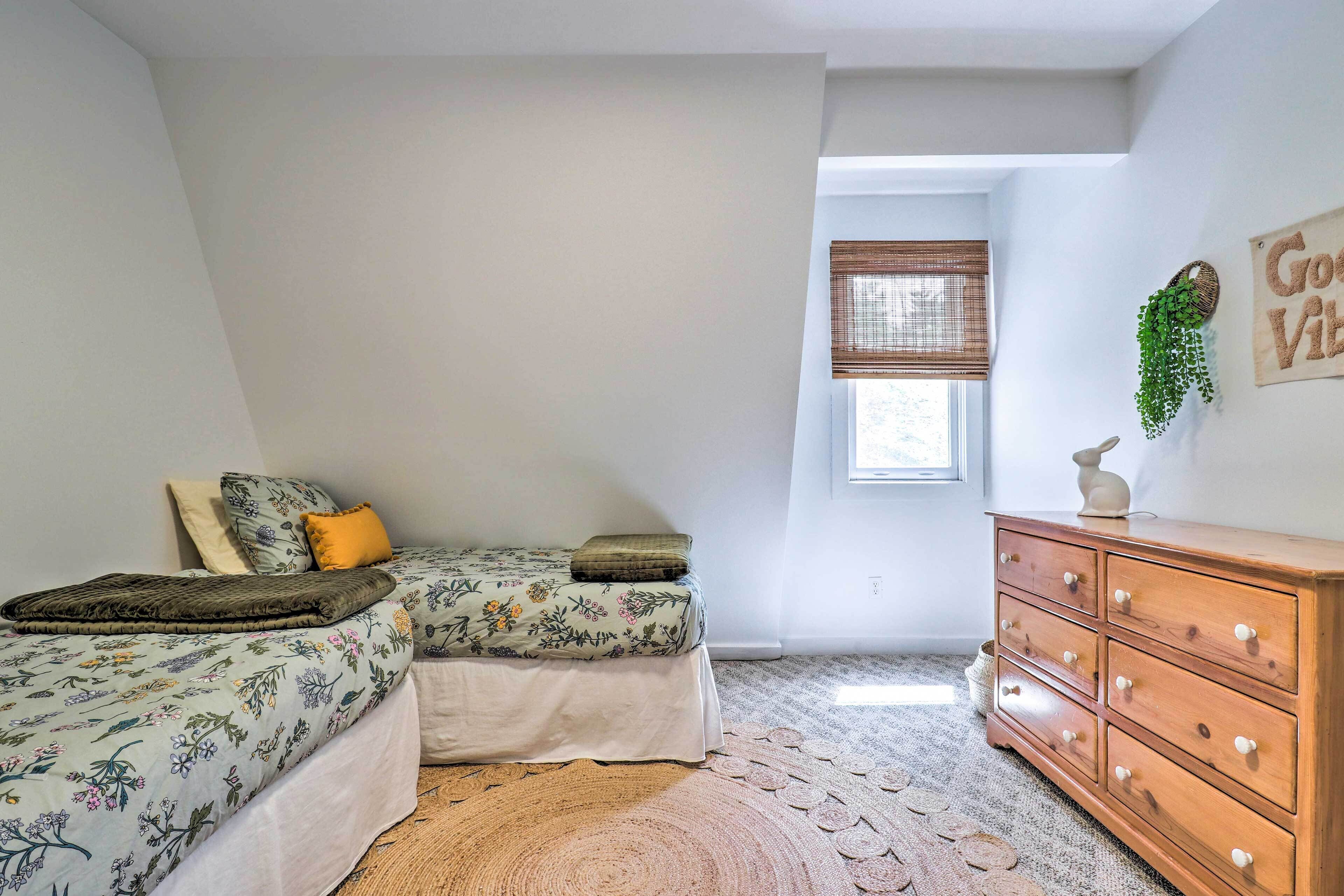 A bedroom with two beds, a dresser, a window, and a wall decoration.