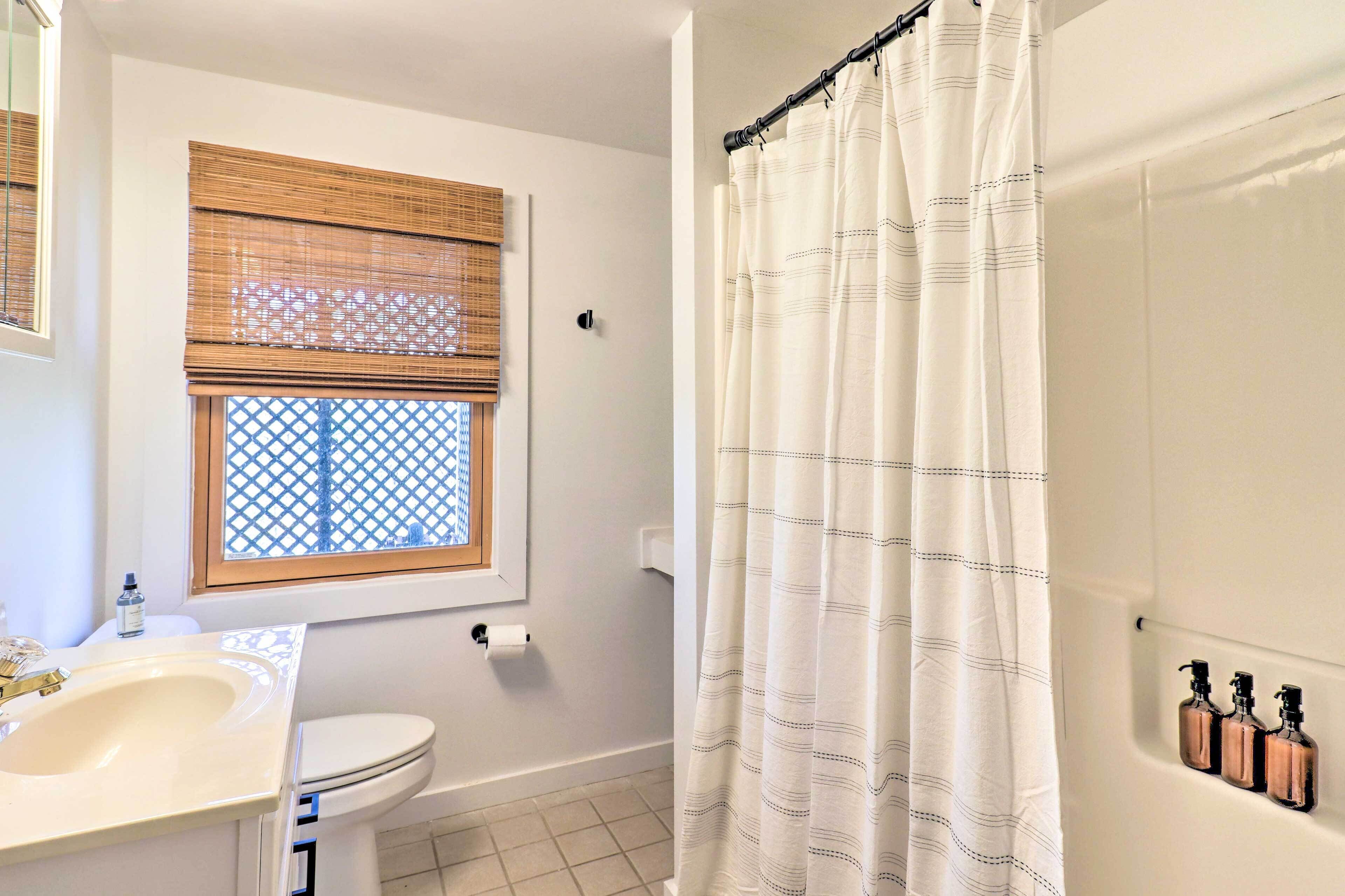 A bathroom with a toilet, sink, window with blinds, and a shower curtain.