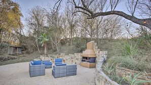 An outdoor patio with stone walls, a barbecue grill, and blue cushioned seating. - Charming Family Cottage Close to San Antonio (Castroville)