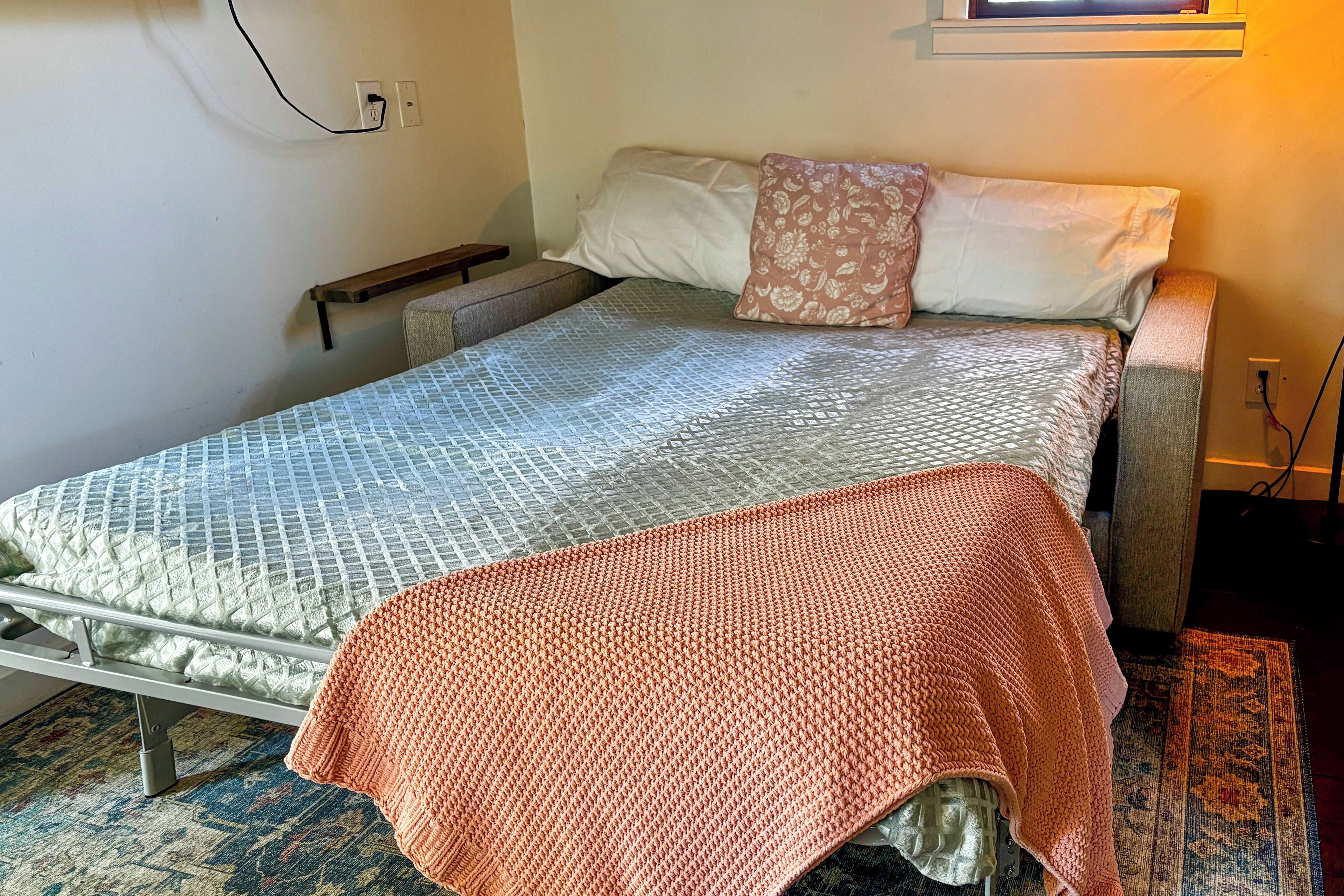 Un lit simple avec une couvre-lit à motifs, une table de chevet et une prise électrique au mur.