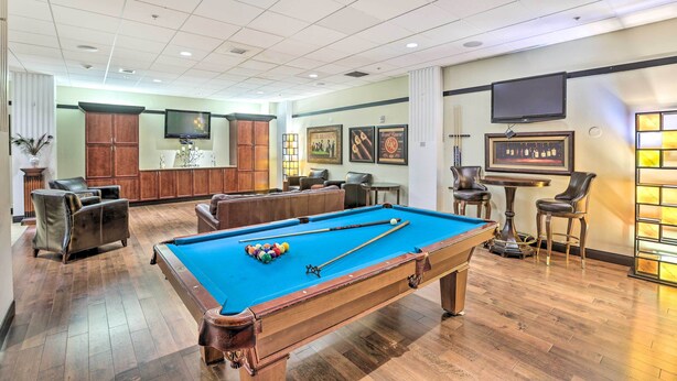 A pool table with a blue felt surface, surrounded by leather chairs and a bar area with stools. - Heart of Dtwn Omaha: Historical Apt w/ Perks (Omaha)