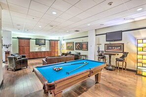 A pool table with a blue felt surface, surrounded by leather chairs and a bar area with stools. - Heart of Dtwn Omaha: Historical Apt w/ Perks (Omaha)