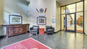A lobby with a wooden cabinet, two leather chairs, a red carpet, and a glass door leading outside. - Heart of Dtwn Omaha: Historical Apt w/ Perks (Omaha)