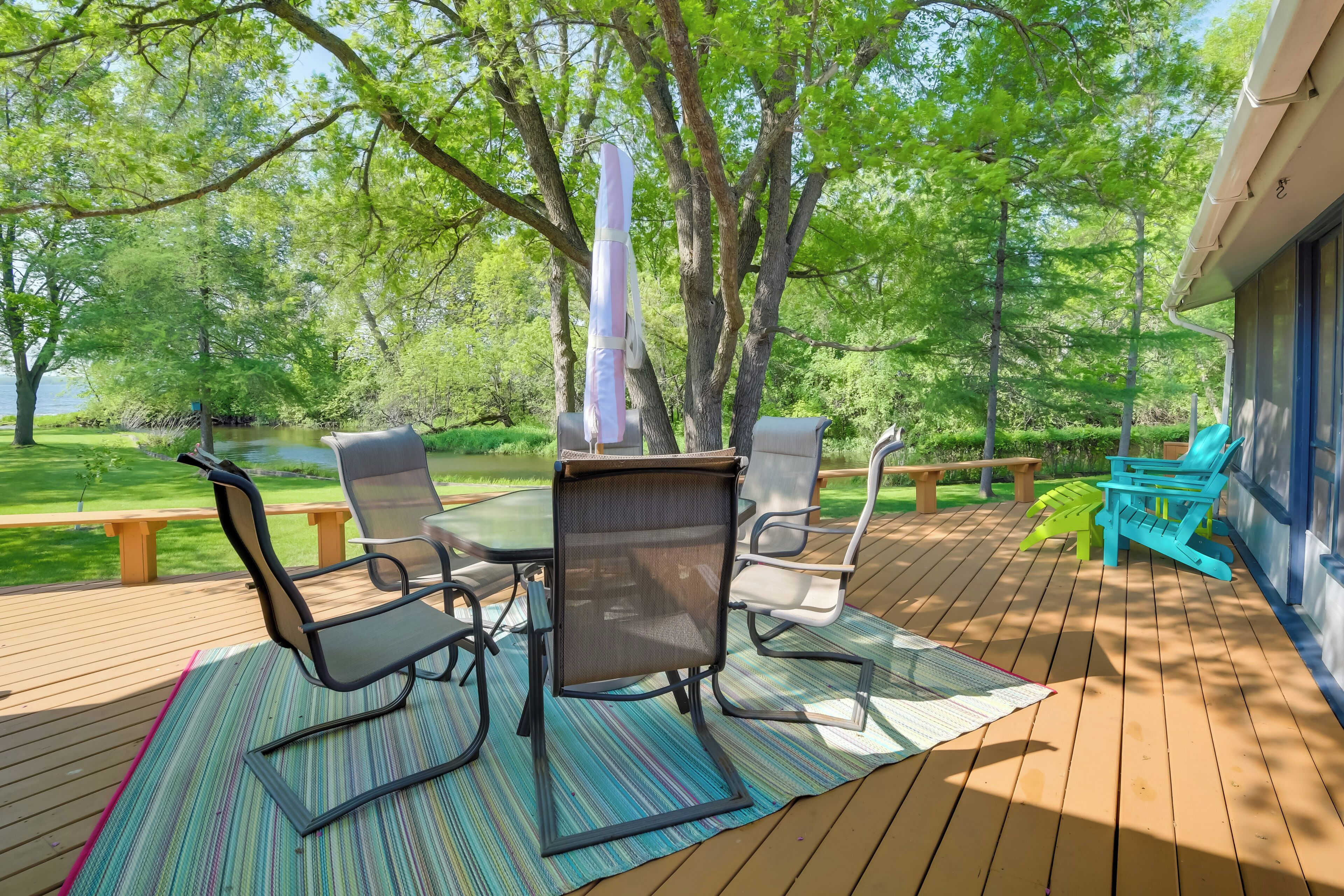 An outdoor deck with a table and chairs, surrounded by trees and a view of a lake.