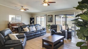 A spacious living room with a leather sofa, a coffee table, and a chair. There is a ceiling fan, a dining table with chairs, and a large window with blinds. - Tuscon Vacation Rental < 1 Mi to Golf Course! (Tucson)