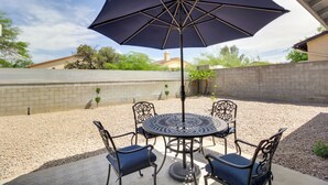 An outdoor patio with a round table and four chairs, an umbrella, and a brick wall in the background. - Tuscon Vacation Rental < 1 Mi to Golf Course! (Tucson)