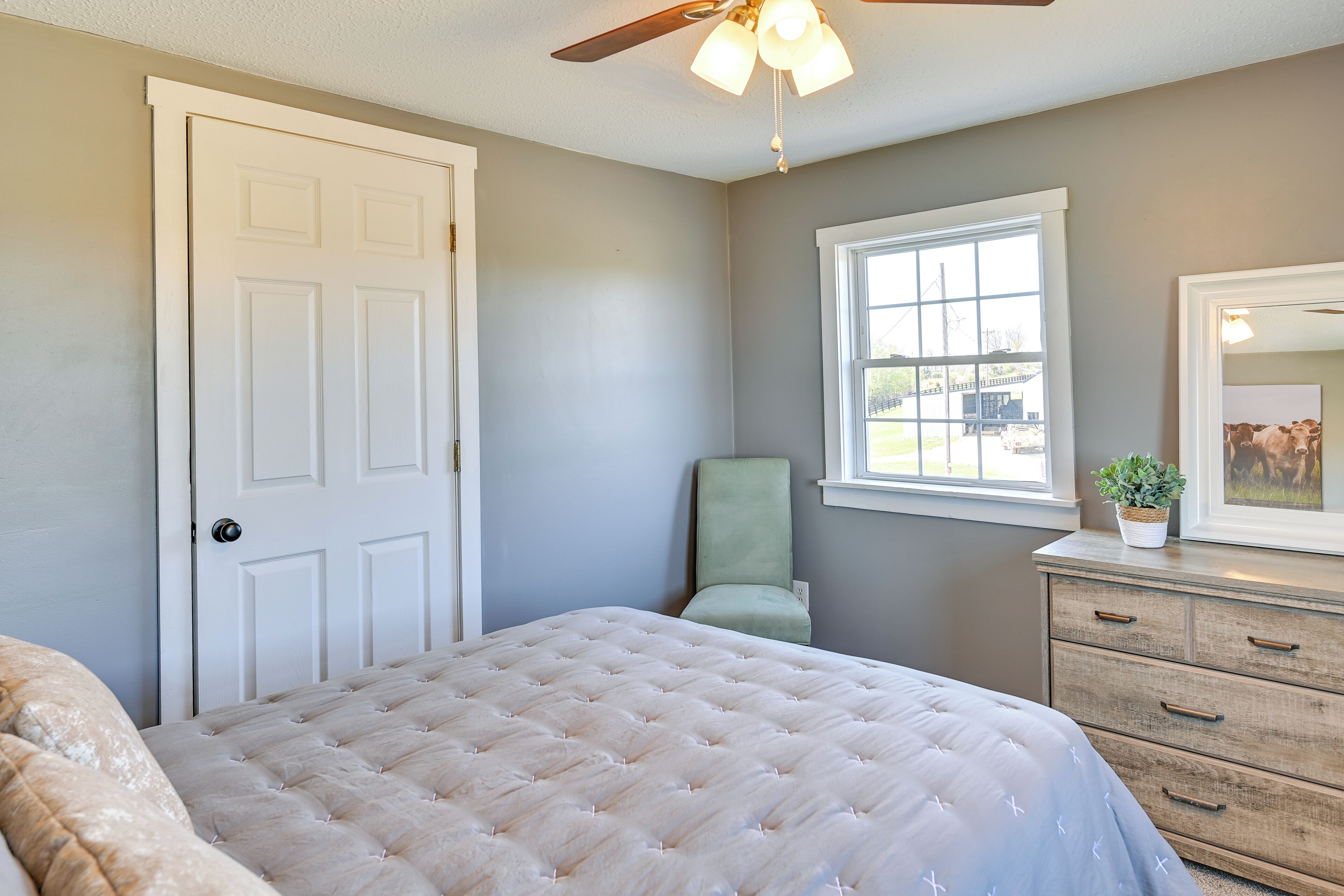 A bedroom with a bed, a dresser, a chair, a window, and a ceiling fan.
