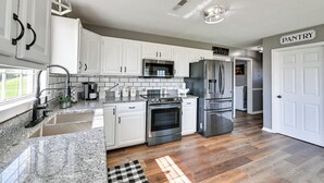 Cocina moderna con armarios blancos, encimeras de granito y electrodomésticos de acero inoxidable, y un cartel que señala la despensa.