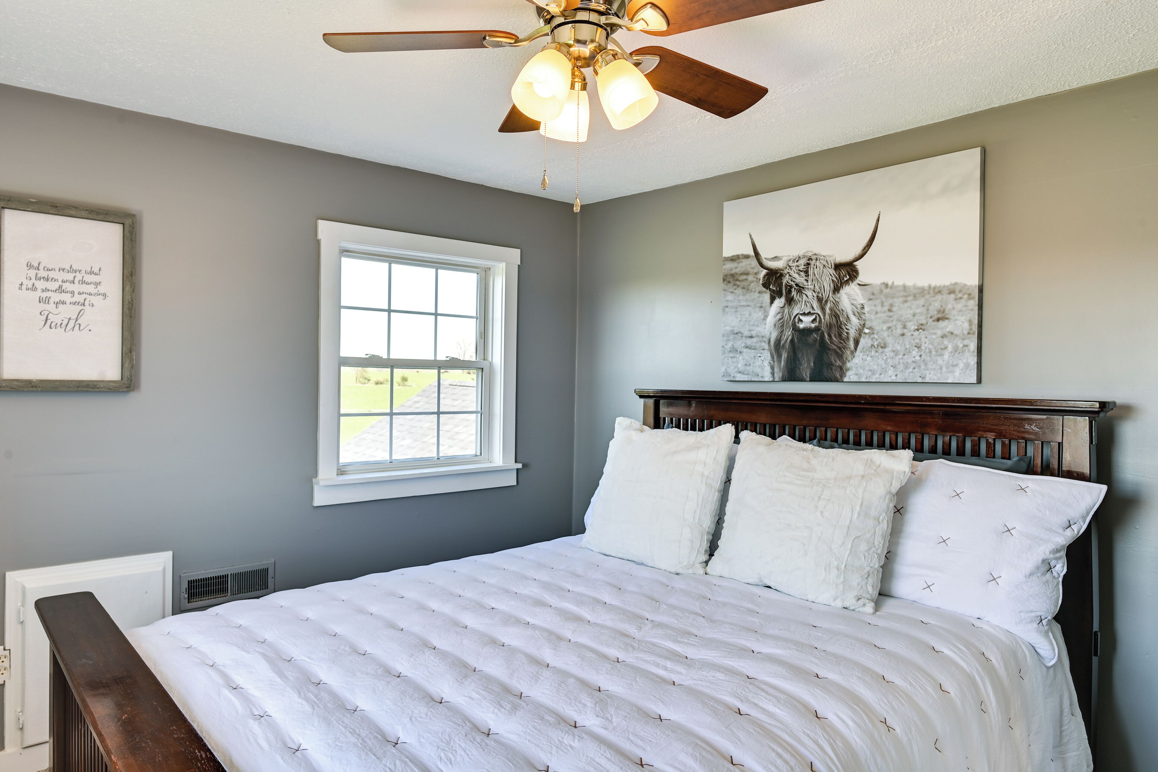 A bedroom with a bed, a ceiling fan, a window, and a framed quote on the wall.