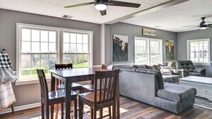 Un amplio espacio habitable con una mesa de comedor, sillas, un sofá seccional gris y un ventilador de techo.