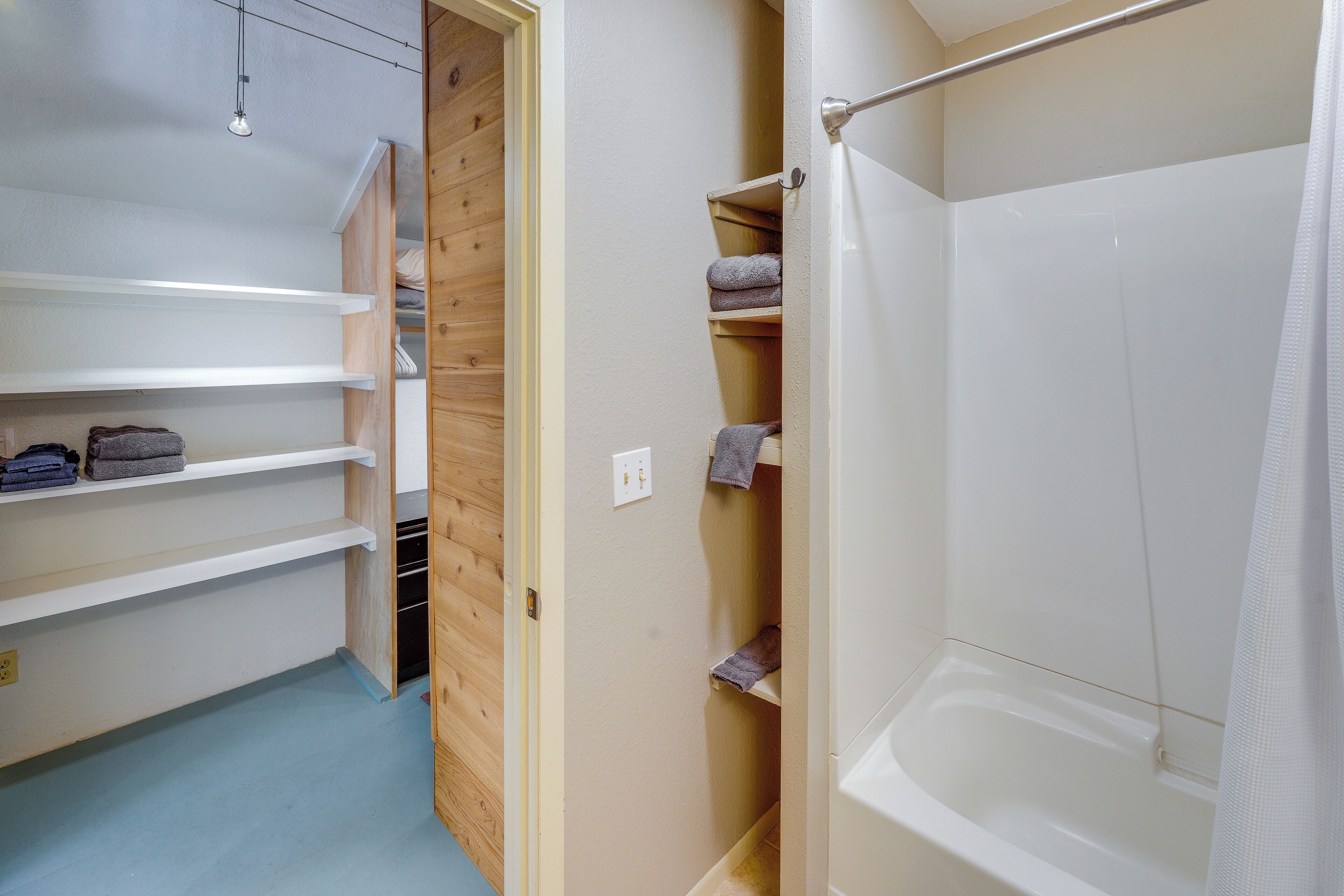 A bathroom with a bathtub, a shower curtain, and shelves with towels.
