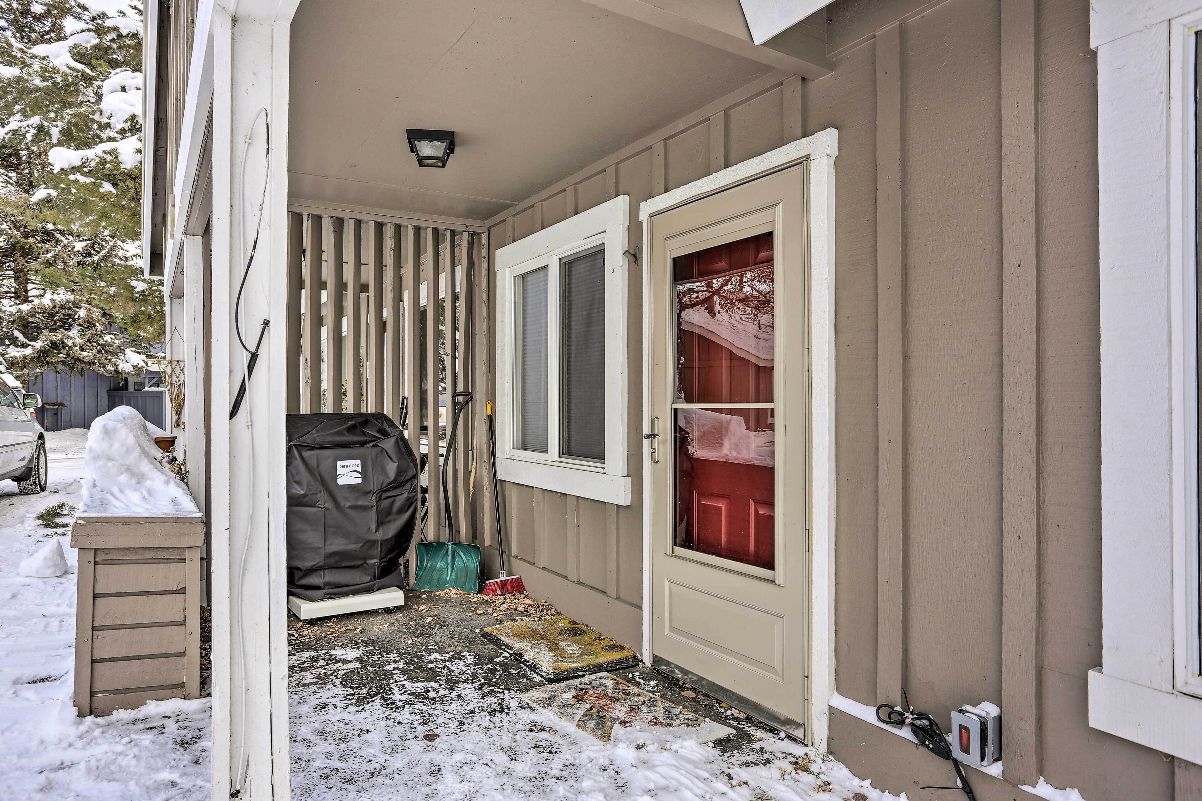A snow-covered entrance with a door, a window, and a covered area with a red door.
