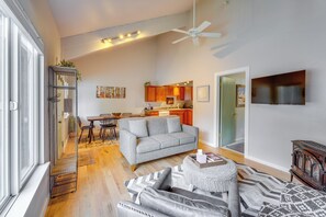 Ein geräumiges Wohnzimmer mit grauem Sofa, einem gemusterten Teppich und einem Deckenventilator.