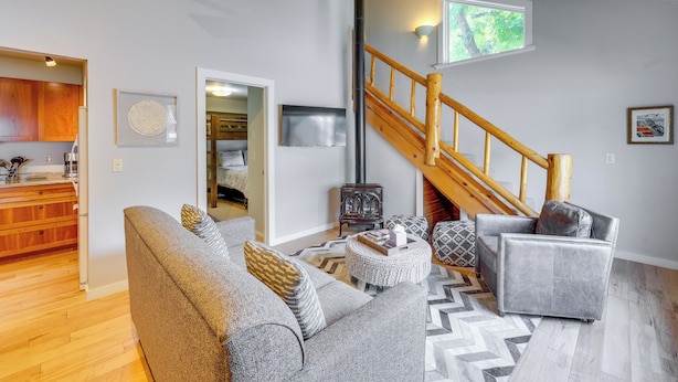 A spacious living room with a gray sofa, a wooden staircase, and a kitchen area. - Ketchum Mountain Retreat: Central Location! (Ketchum)