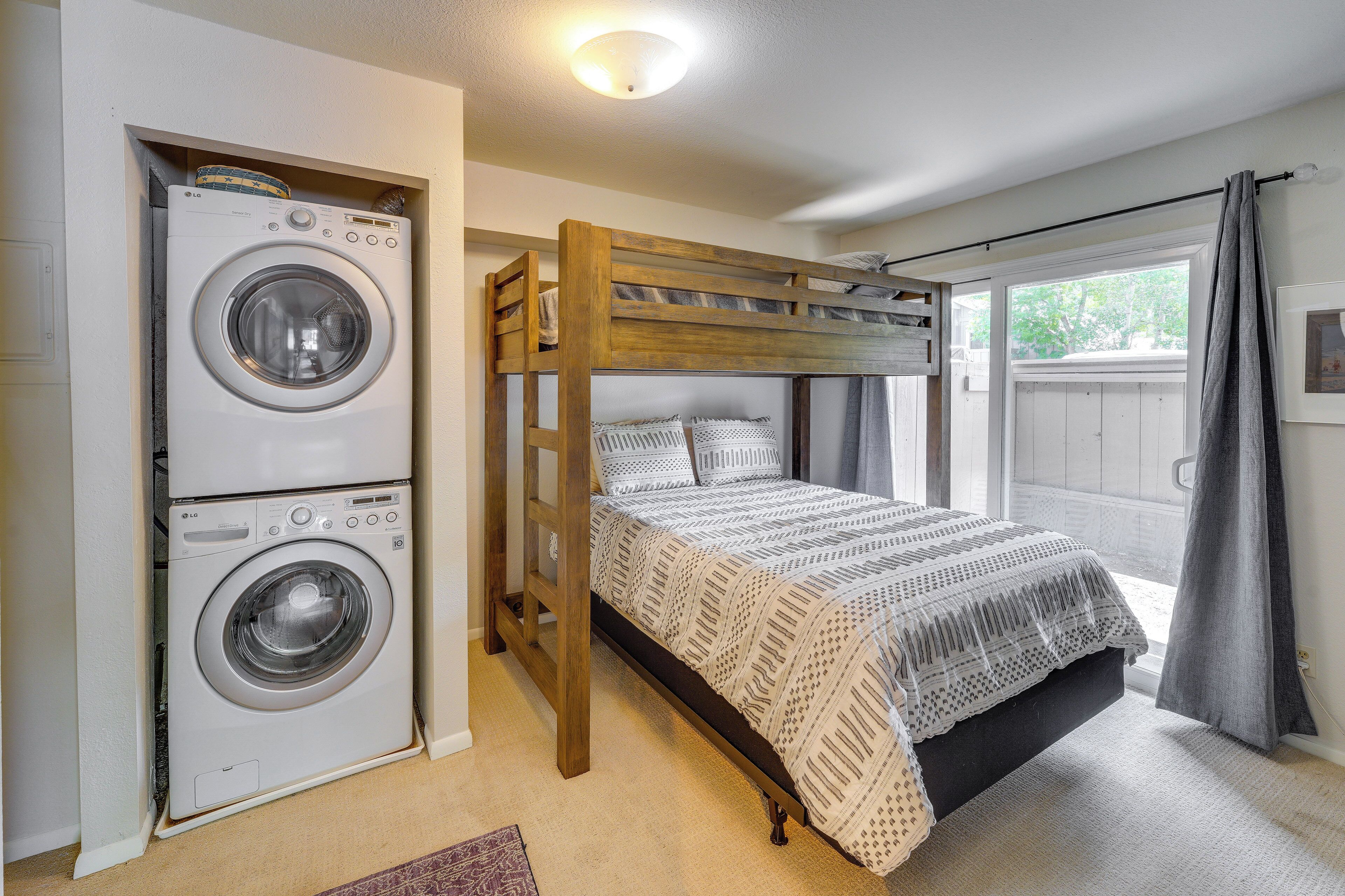 Een kleine kamer met een stapelbed, een wasmachine en een raam met gordijnen.