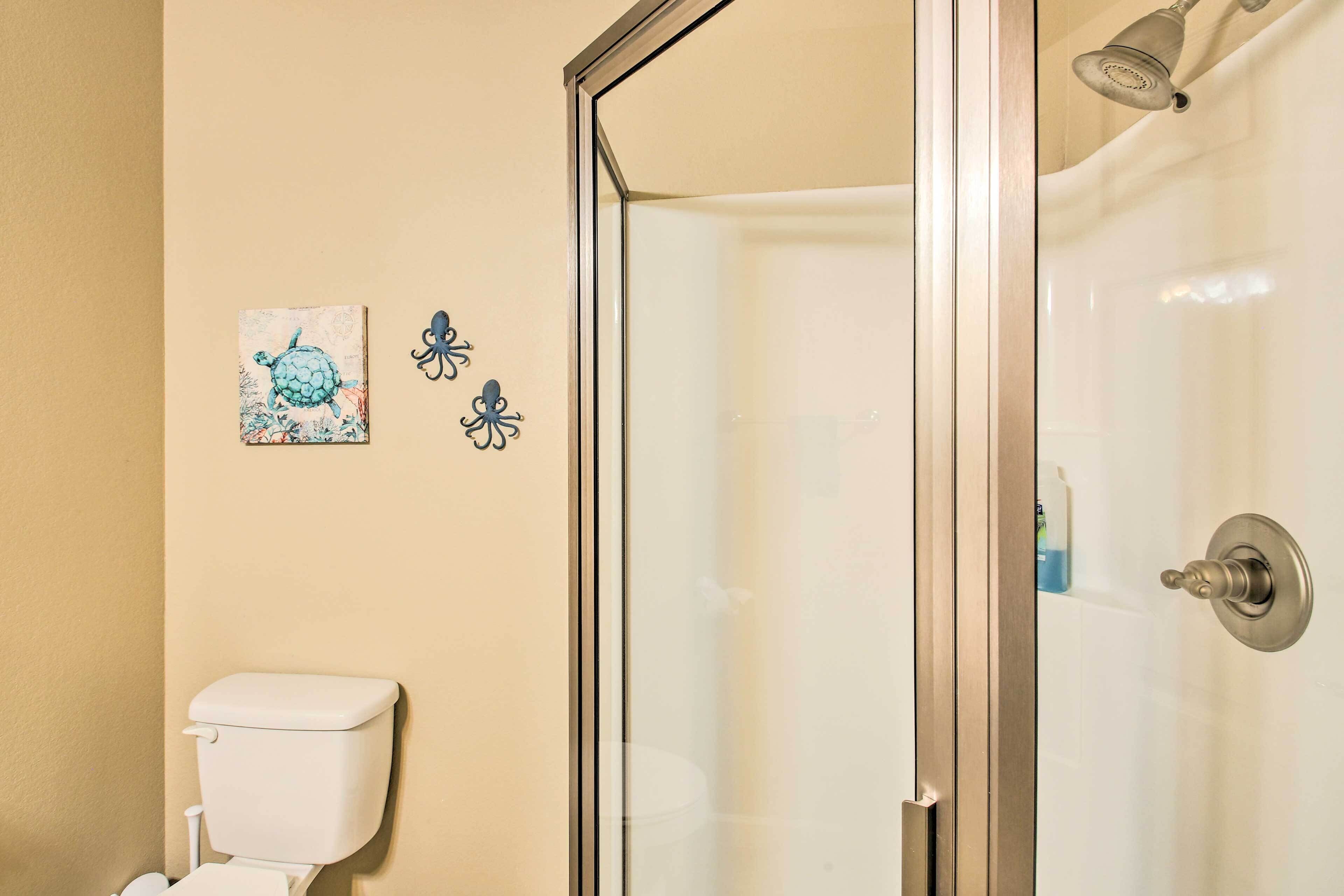 A bathroom with a toilet, a glass shower enclosure, and two wall decorations.
