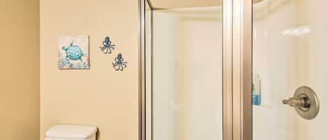 A bathroom with a toilet, a glass shower enclosure, and two wall decorations.