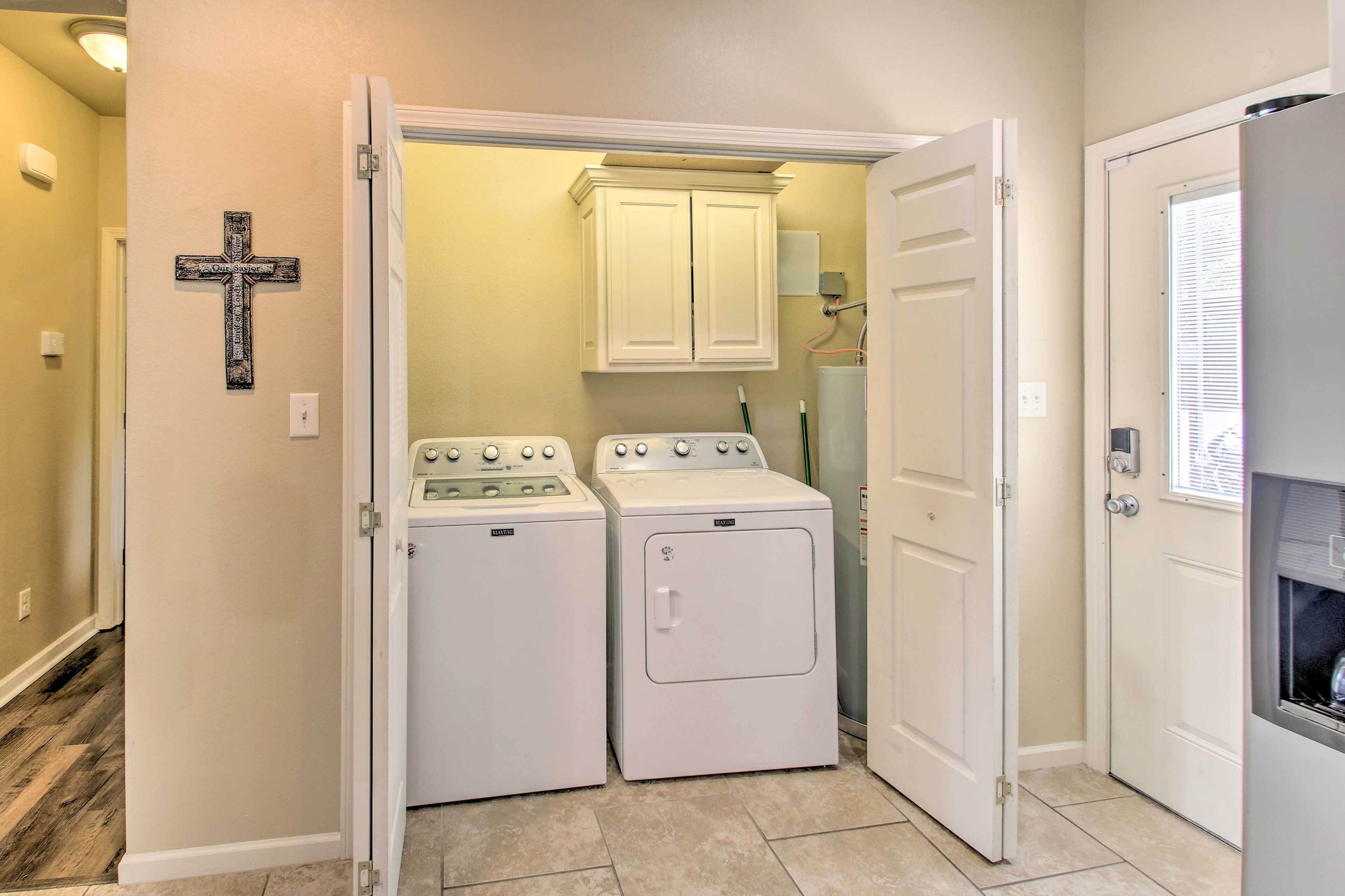 A laundry room with two washers and a dryer, a white cross on the wall, and a cabinet above the dryers.