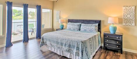 A bedroom with a large bed, two bedside tables, a ceiling fan, and a view of a balcony.