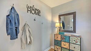 En gang med et 'Welcome Home'-skilt, et knagered med jakker, en lampe og et spejl over et flerfarvet skab.