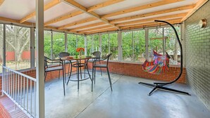 En overdækket terrasse med et bord og stole, en hængekøjsstol og en murstensmur.
