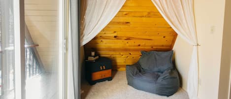 A cozy room with a wooden ceiling, a gray bean bag, a small dresser, and sheer curtains.