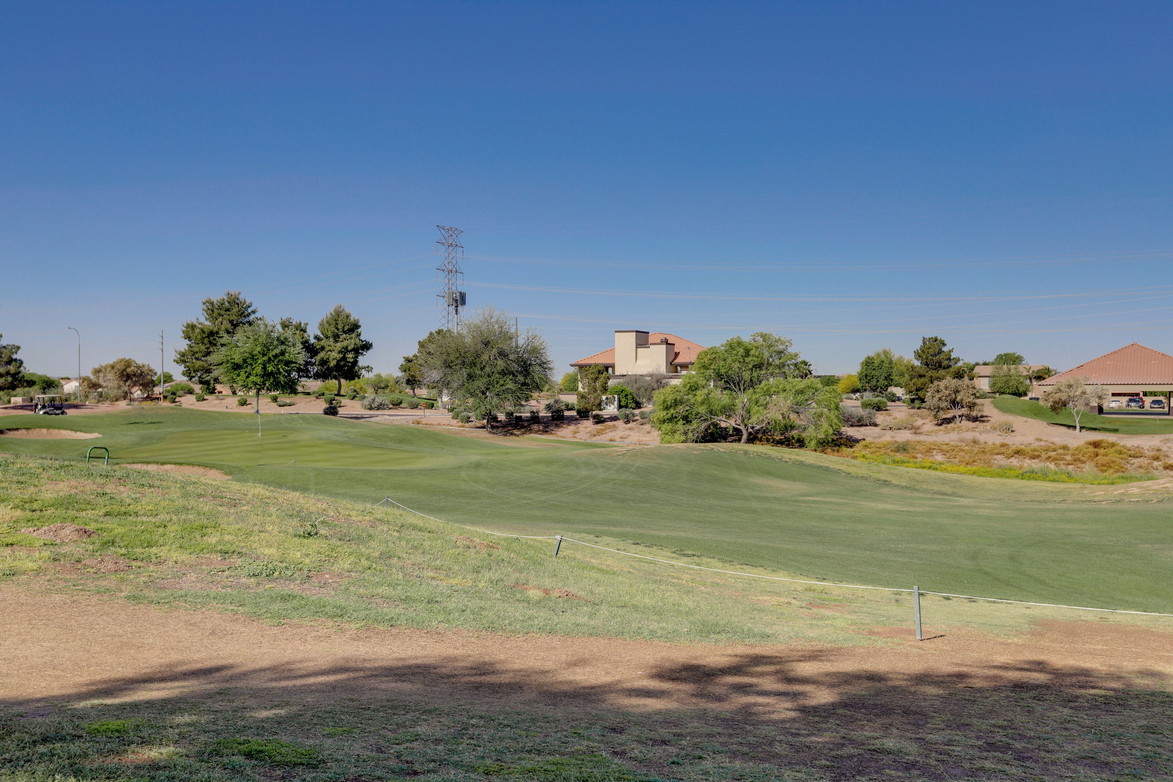 Ein Golfplatz unter blauem Himmel, mit vereinzelten Bäumen und einem Gebäude im Hintergrund.