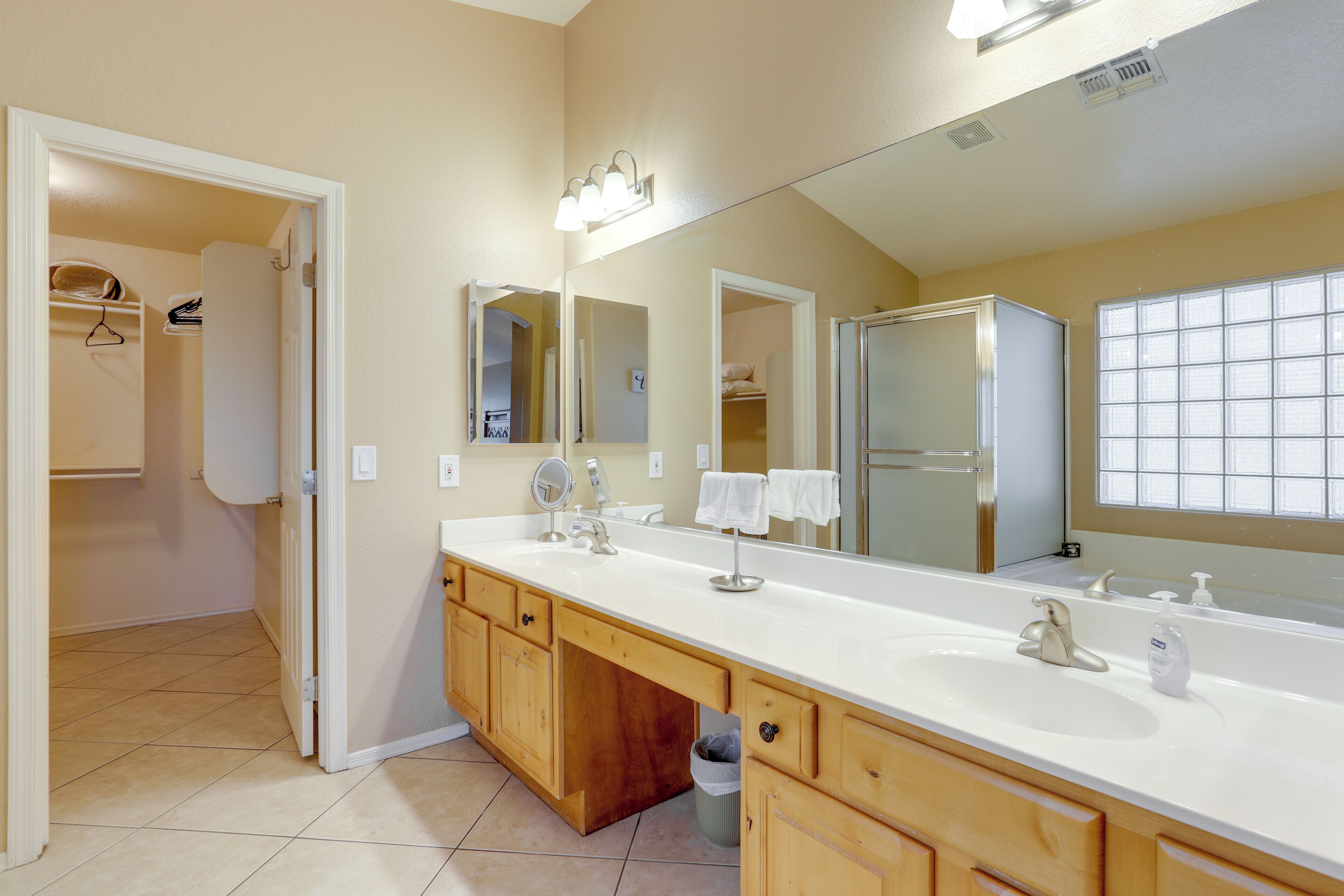 A bathroom with a large mirror, a double sink, wooden cabinets, and a walk-in closet.