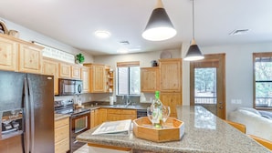 A modern kitchen with wooden cabinets, granite countertops, stainless steel appliances, and a central island with a wine glass and bottle. - Golf Course View: Torreon Vacation Rental! (Show Low)