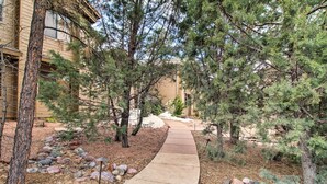 A pathway lined with trees and rocks, leading to a building with a beige exterior. - Golf Course View: Torreon Vacation Rental! (Show Low)