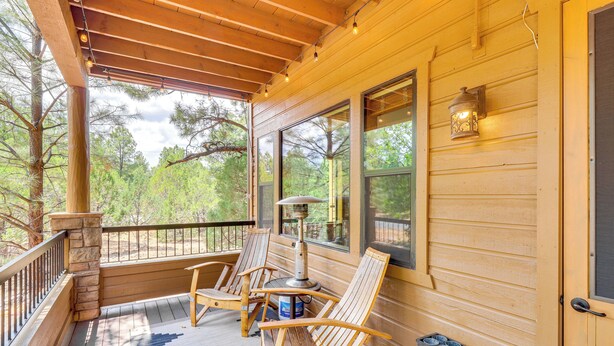 A wooden porch with two Adirondack chairs, a table, and a lantern. - Golf Course View: Torreon Vacation Rental! (Show Low)
