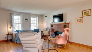 A cozy living room with a fireplace, a television mounted above it, and a striped sofa. - Walk to Village! Family-friendly Gem in East Burke (East Burke)