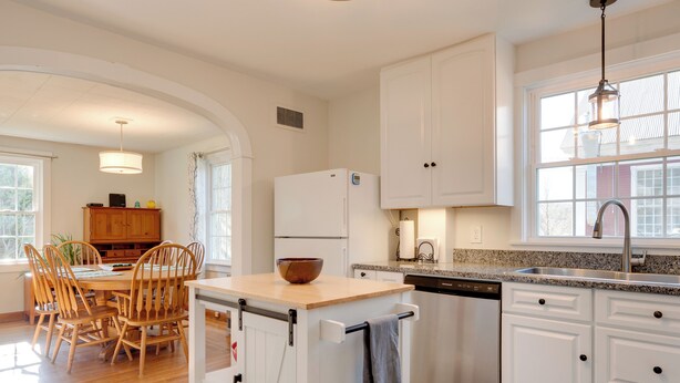 A kitchen with white cabinets, a wooden dining table with chairs, a refrigerator, and a dishwasher. - Walk to Village! Family-friendly Gem in East Burke (East Burke)