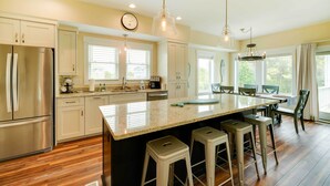 A modern kitchen with a large island, bar stools, and a dining area with a chandelier. - Corolla Vacation Rental w/ Pool, Walk to Beach! (Corolla)