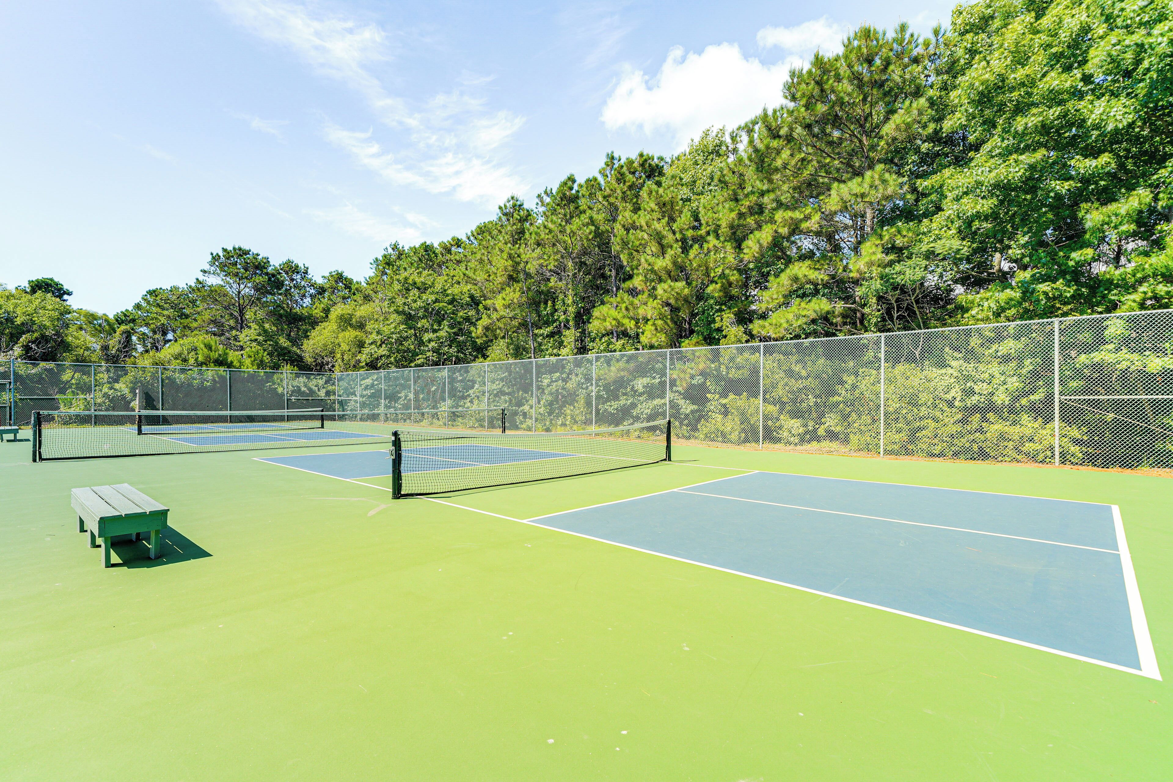 Un campo da tennis all'aperto con superficie verde e blu, circondato da una recinzione e alberi.