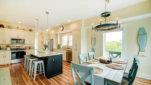A spacious kitchen with a central island, wooden flooring, and a dining area with a table set for four. - Corolla Vacation Rental w/ Pool, Walk to Beach! (Corolla)