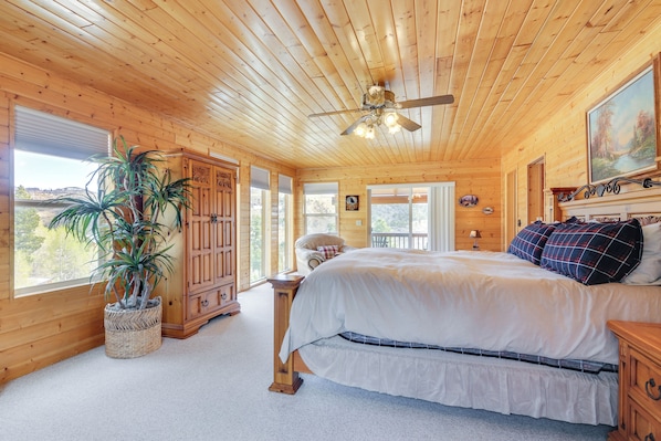 Quarto de cabana de madeira com cama, ventilador de teto, janela grande e planta em vaso.