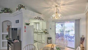 A dining area with a wooden table, white chairs, and a chandelier. There is a kitchen in the background with white cabinets and a sink. - 2 Mi to Lake Havasu: Peaceful Home w/ Pool & Views (Lake Havasu City)