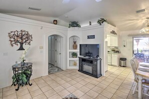 A spacious living room with a TV, decorative plants, and a dining area with a table and chairs.