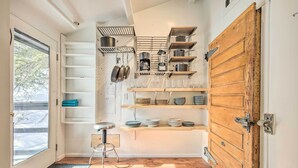 A compact kitchen with wooden shelves, a bar stool, and a large wooden door. - Relaxing Cuchara Retreat on Cucharas River w/ View (La Veta)