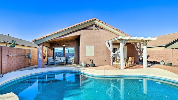 Ein Schwimmbad mit überdachter Terrasse, ein Backsteinhaus und ein klarer, blauer Himmel.