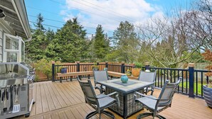 A deck with a grill, a table with chairs, and a view of trees and a wooden fence. - Home w/ Hot Tub: 7 Mi to Edmonds Waterfront! (Lynnwood)