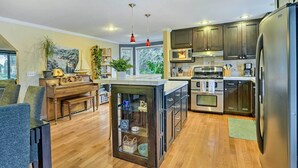 A modern kitchen with wooden cabinets, a central island, and a built-in microwave. - Home w/ Hot Tub: 7 Mi to Edmonds Waterfront! (Lynnwood)